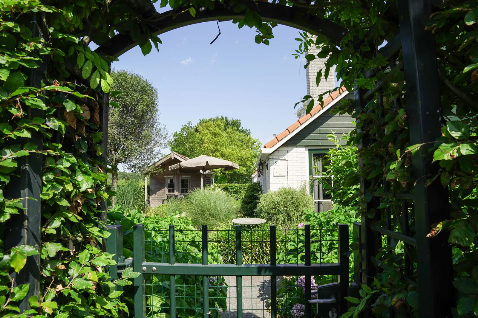 Doorkijk door de begroeide poort naar de omheinde tuin en het tuinhuis van vakantiewoning Nachtegaal, Appelscha